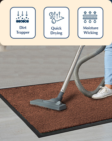 Indoor doormat with brown surface being vacuumed. Icons above show features: dirt trapping, quick drying, and moisture wicking capabilities.